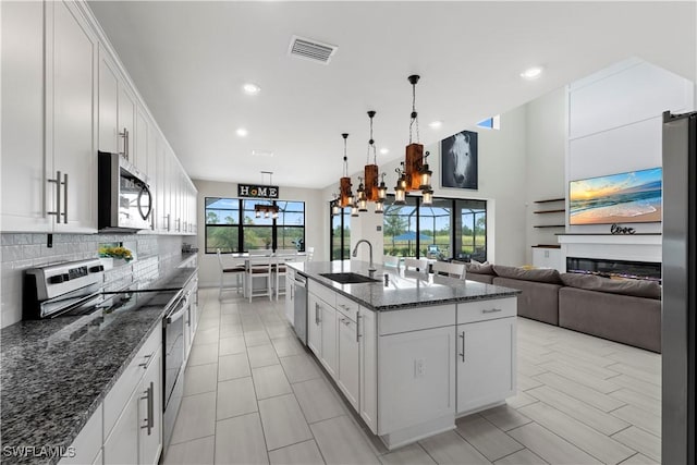 kitchen with dark stone counters, a center island with sink, sink, appliances with stainless steel finishes, and white cabinetry