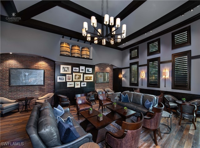 cinema room featuring dark wood-type flooring, beamed ceiling, brick wall, a towering ceiling, and a chandelier