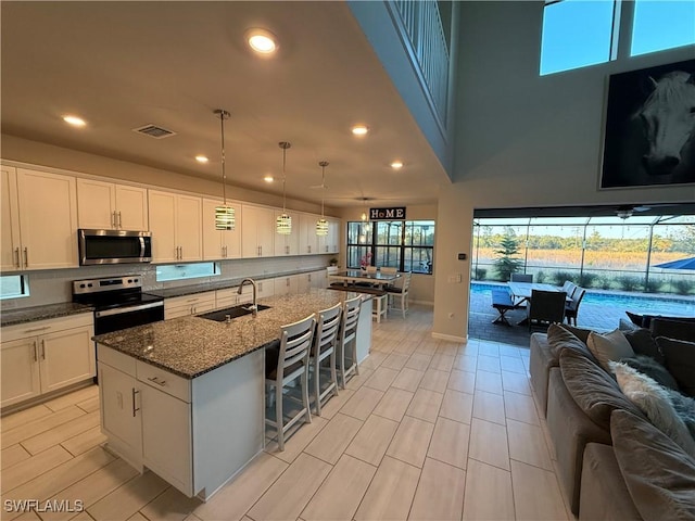 kitchen featuring sink, pendant lighting, stainless steel appliances, a kitchen island with sink, and white cabinets