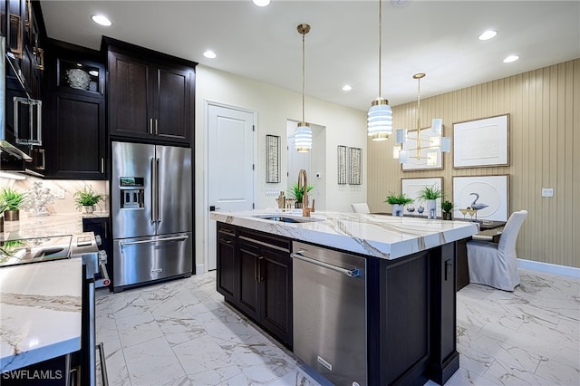 kitchen with a center island with sink, light stone counters, sink, pendant lighting, and stainless steel appliances