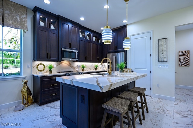 kitchen featuring a center island with sink, a breakfast bar area, appliances with stainless steel finishes, backsplash, and pendant lighting