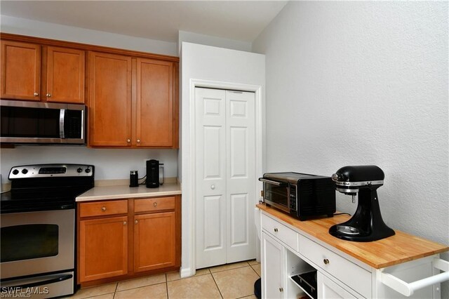 kitchen with appliances with stainless steel finishes, wood counters, and light tile patterned flooring