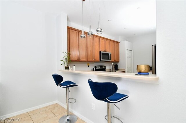 kitchen featuring light tile patterned floors, a kitchen bar, hanging light fixtures, kitchen peninsula, and sink