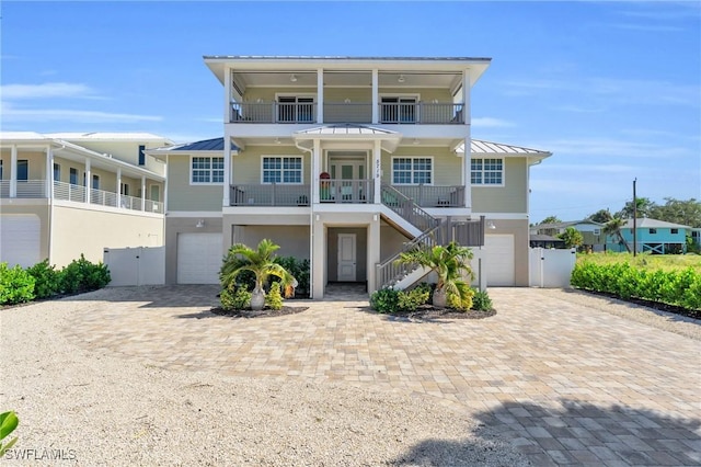 coastal inspired home featuring decorative driveway, a standing seam roof, stairway, and an attached garage