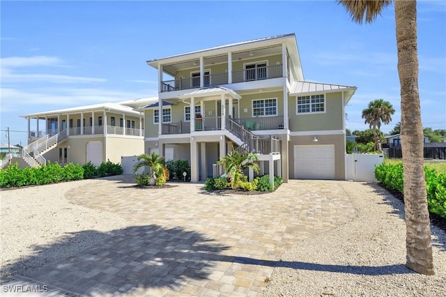 coastal home with decorative driveway, a standing seam roof, metal roof, a garage, and stairs