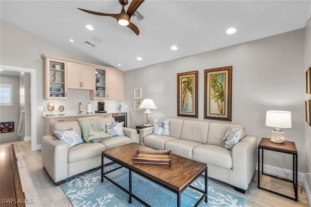 living area with a ceiling fan, visible vents, vaulted ceiling, and light wood finished floors