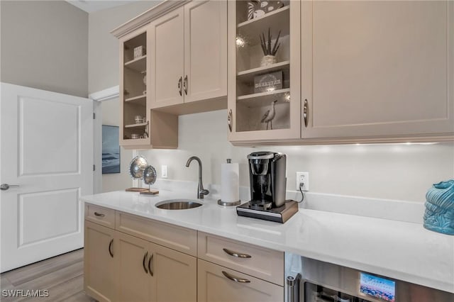 kitchen featuring wine cooler, light wood-style flooring, a sink, light countertops, and glass insert cabinets