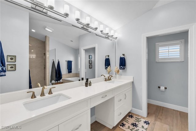 bathroom with double vanity, baseboards, lofted ceiling, wood finished floors, and a sink