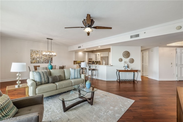 living room with crown molding, dark hardwood / wood-style flooring, and ceiling fan with notable chandelier