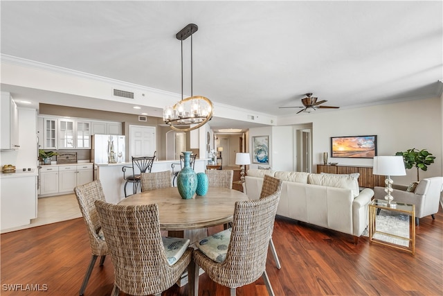 dining area featuring dark wood-type flooring, ornamental molding, and ceiling fan with notable chandelier