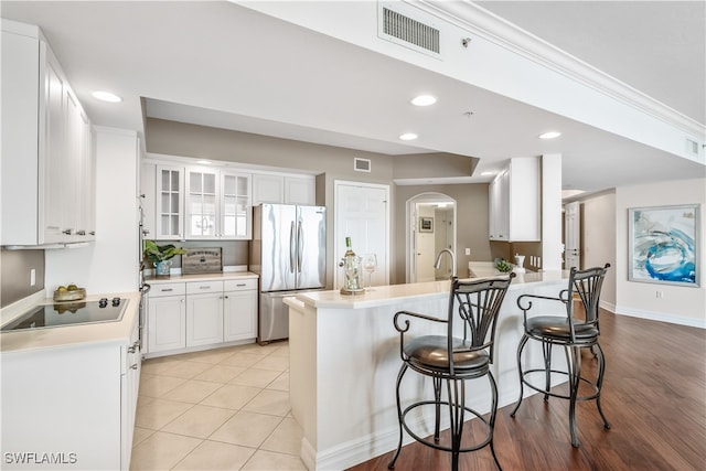 kitchen with black electric stovetop, kitchen peninsula, stainless steel fridge, a breakfast bar, and white cabinets