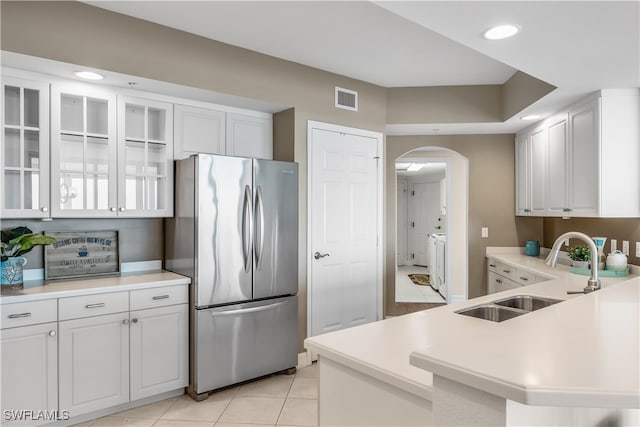 kitchen featuring white cabinets, sink, light tile patterned floors, and stainless steel refrigerator