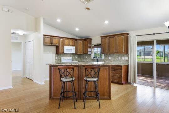 kitchen featuring white appliances, backsplash, vaulted ceiling, light stone countertops, and light hardwood / wood-style floors