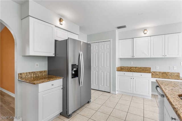 kitchen with stainless steel fridge, light tile patterned floors, stone countertops, and white cabinets