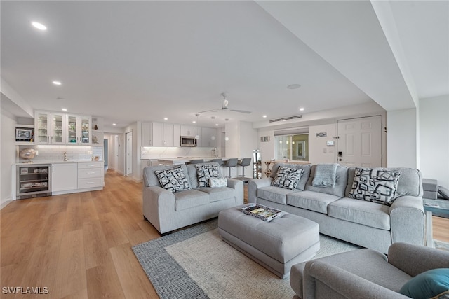 living room with bar area, ceiling fan, wine cooler, and light wood-type flooring