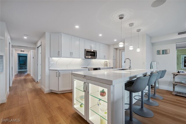 kitchen featuring light wood-type flooring, pendant lighting, white cabinetry, and sink