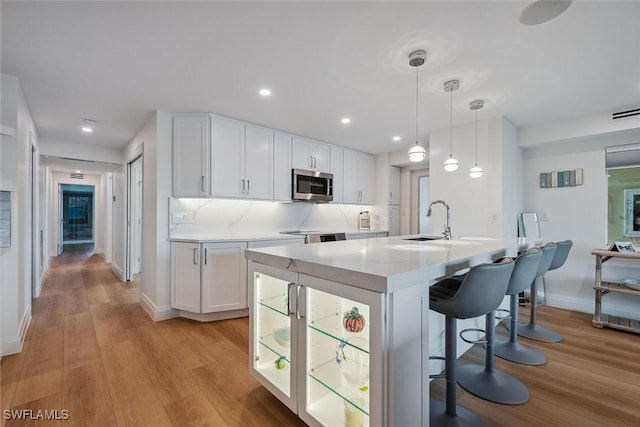 kitchen with tasteful backsplash, stainless steel microwave, a breakfast bar area, white cabinets, and a sink