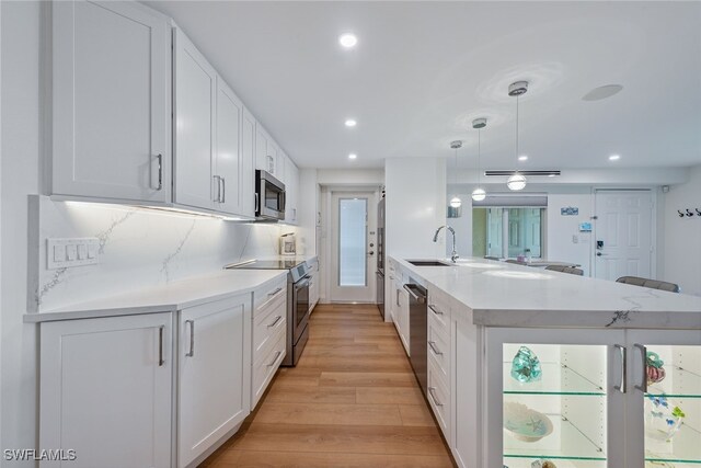 kitchen featuring light wood-type flooring, pendant lighting, stainless steel appliances, kitchen peninsula, and white cabinets