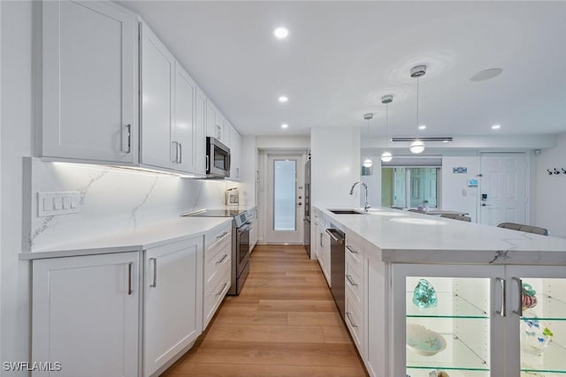 kitchen with a peninsula, light wood-style flooring, stainless steel appliances, white cabinets, and tasteful backsplash