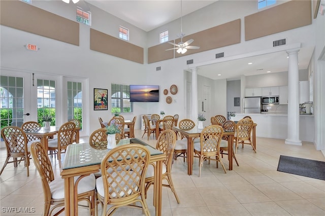 dining space with ornate columns, a towering ceiling, light tile patterned floors, and ceiling fan