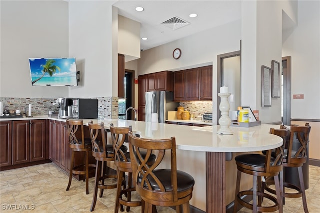 kitchen with stainless steel fridge, a kitchen bar, backsplash, and kitchen peninsula