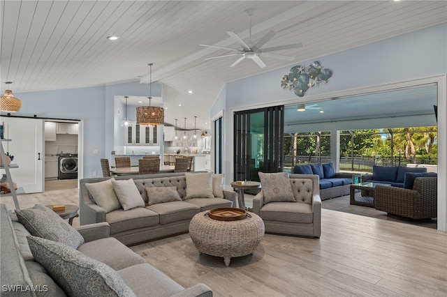 living room with light hardwood / wood-style floors, lofted ceiling with beams, washer / clothes dryer, a barn door, and ceiling fan with notable chandelier