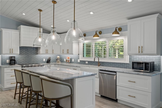 kitchen with appliances with stainless steel finishes, decorative backsplash, white cabinetry, vaulted ceiling, and a center island