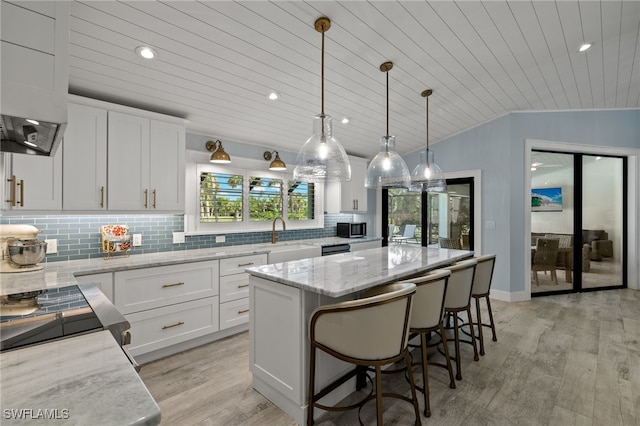 kitchen featuring pendant lighting, a kitchen island, lofted ceiling, and white cabinetry