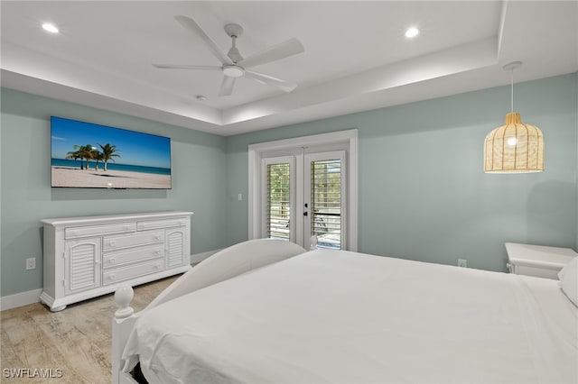 bedroom with ceiling fan, light hardwood / wood-style floors, access to exterior, and a tray ceiling