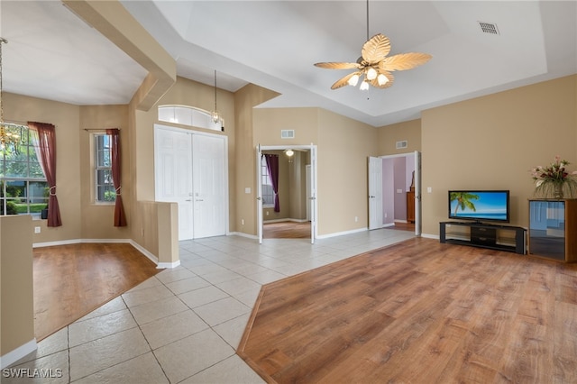 unfurnished living room featuring ceiling fan with notable chandelier, light tile patterned floors, and a tray ceiling