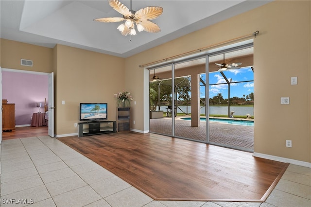 unfurnished living room featuring light tile patterned flooring, ceiling fan, and a raised ceiling