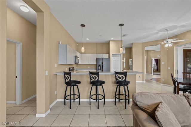 kitchen with a kitchen breakfast bar, kitchen peninsula, light tile patterned floors, stainless steel fridge, and decorative light fixtures