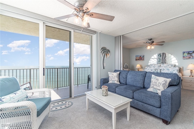 carpeted living room with ceiling fan, a textured ceiling, and a water view