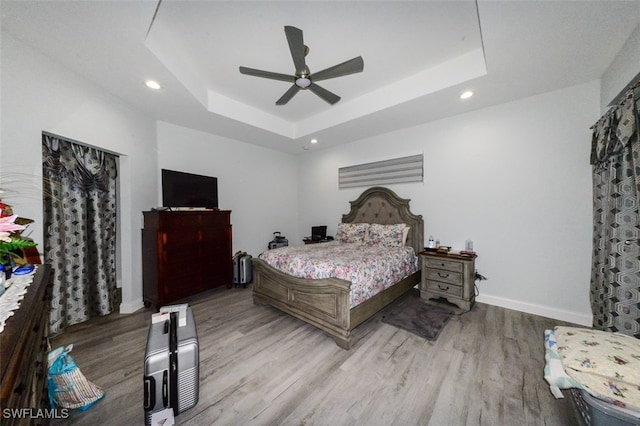 bedroom with ceiling fan, light hardwood / wood-style floors, and a raised ceiling