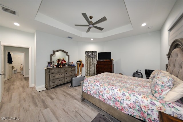 bedroom featuring ceiling fan, light wood-type flooring, and a tray ceiling