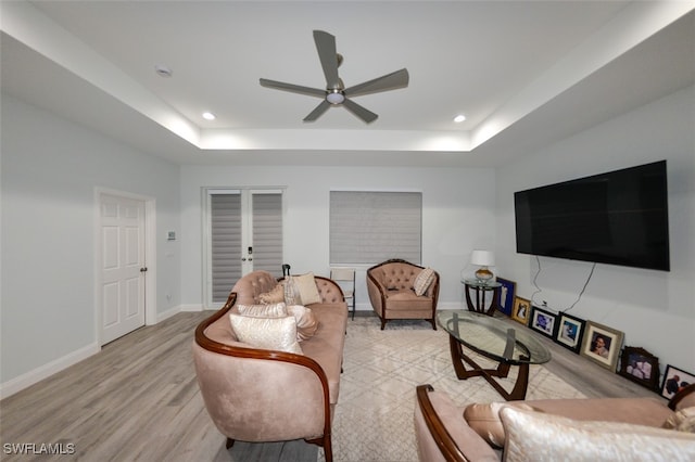 living room with ceiling fan, a raised ceiling, and light hardwood / wood-style flooring