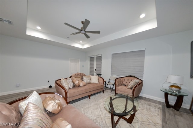 living room with ceiling fan, a tray ceiling, and light hardwood / wood-style flooring