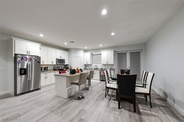 kitchen featuring stainless steel appliances, white cabinets, a kitchen island, and light wood-type flooring