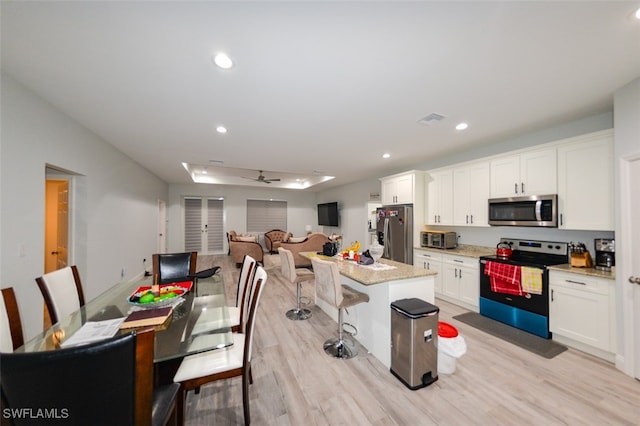 kitchen with ceiling fan, white cabinets, appliances with stainless steel finishes, a center island, and light wood-type flooring