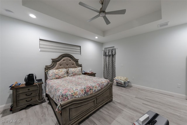 bedroom with light wood-type flooring, ceiling fan, and a raised ceiling