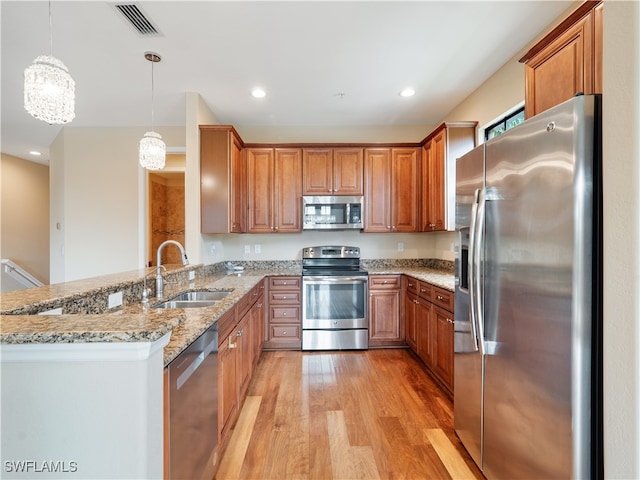 kitchen with light hardwood / wood-style flooring, stainless steel appliances, kitchen peninsula, sink, and hanging light fixtures