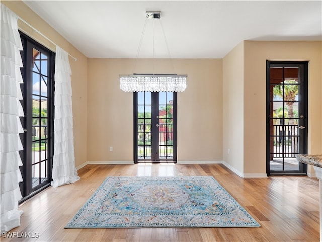 interior space featuring a wealth of natural light, a notable chandelier, light wood-type flooring, and french doors