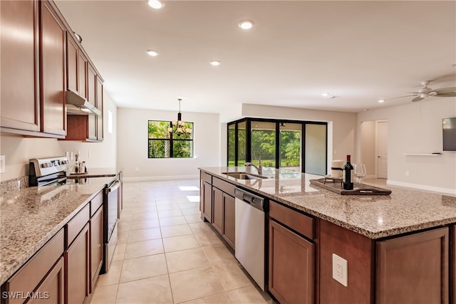 kitchen with light stone counters, a kitchen island with sink, stainless steel appliances, sink, and decorative light fixtures