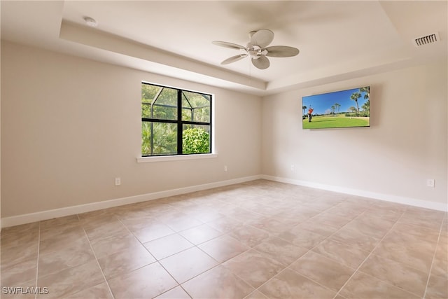 spare room featuring ceiling fan, light tile patterned flooring, and a tray ceiling