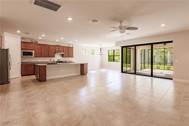 kitchen with light stone countertops, light tile patterned flooring, ceiling fan with notable chandelier, stainless steel appliances, and a kitchen island with sink