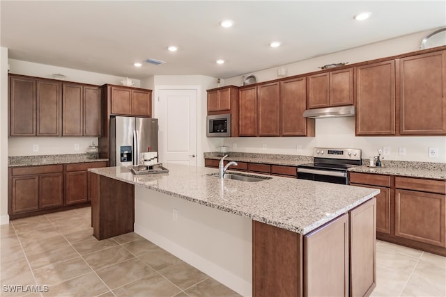 kitchen with a kitchen island with sink, sink, light tile patterned floors, appliances with stainless steel finishes, and light stone counters