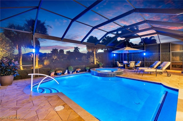 pool at dusk featuring glass enclosure, an in ground hot tub, and a patio