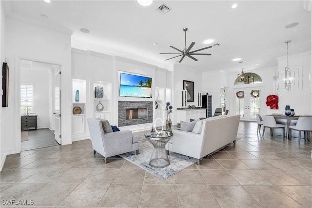 living room featuring french doors, ornamental molding, ceiling fan, built in features, and a stone fireplace