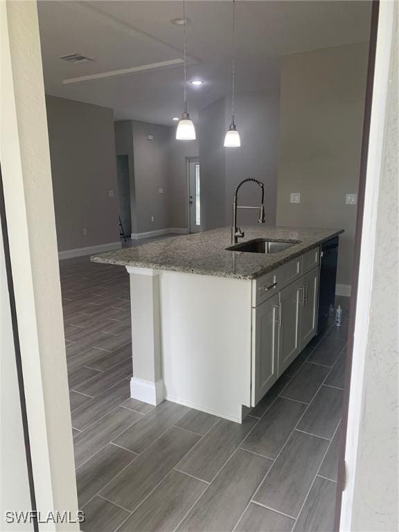 kitchen with wood finish floors, light stone countertops, pendant lighting, dishwasher, and a sink