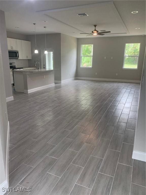 unfurnished living room featuring visible vents, a sink, baseboards, ceiling fan, and wood tiled floor